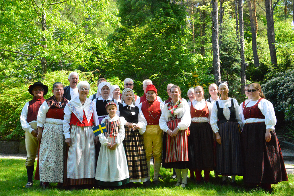 Medlemmarna i Enköpings folkdansgille står iklädda folkdräkter ute i naturen, bild.