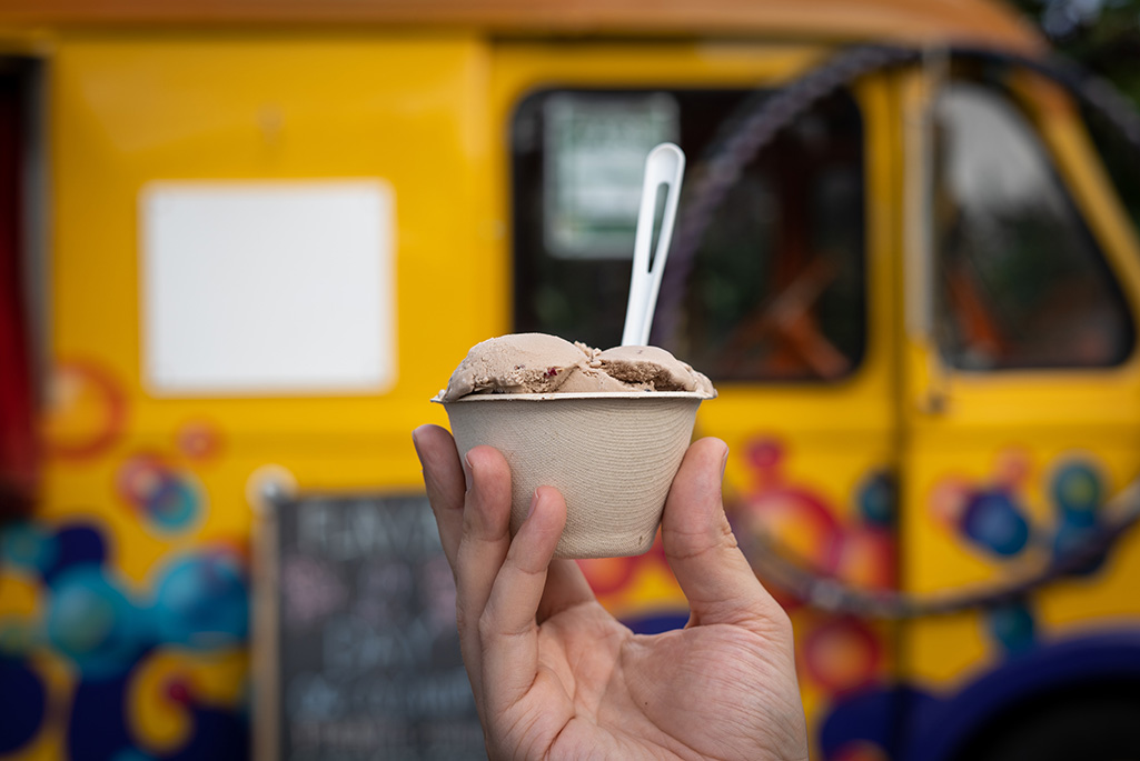 Foto på en persons hand som håller i en glass i bägare utanför en vagn som säljer mat.