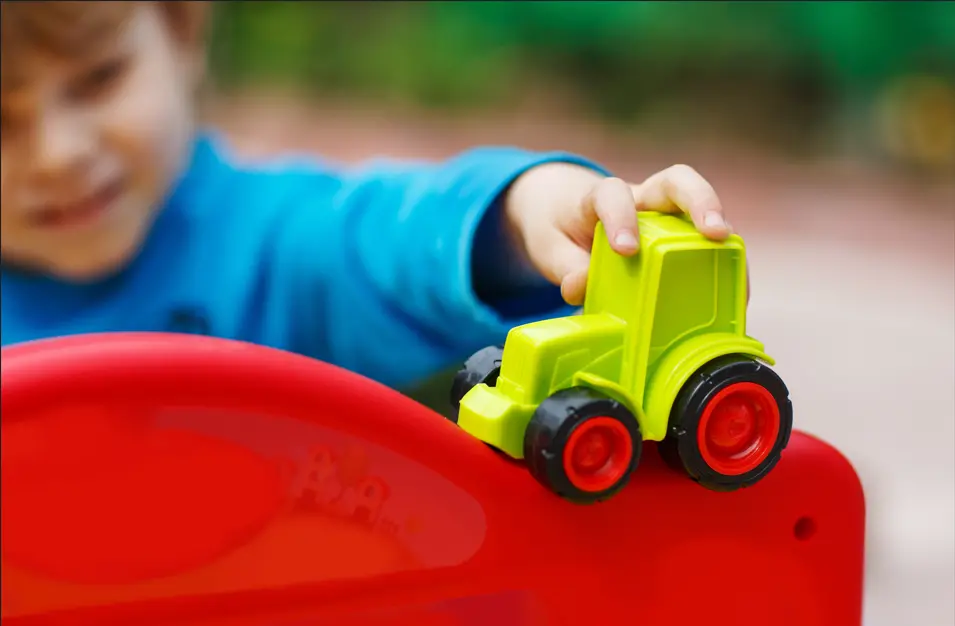 Barn håller grön traktor i plast