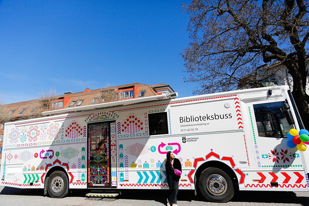 Bild på biblioteksbussen i Enköping och Saadia Husein som skapat konstverket som syns utanpå bussen.