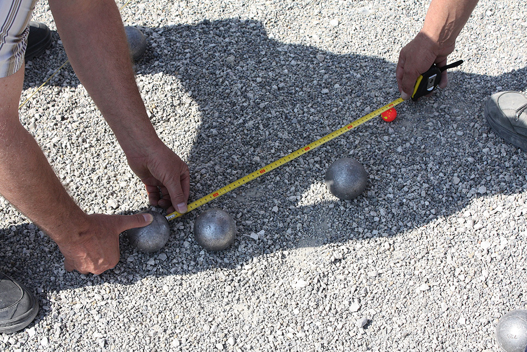 Bild på boulespelare som mäter avstånd mellan boulekulorna.