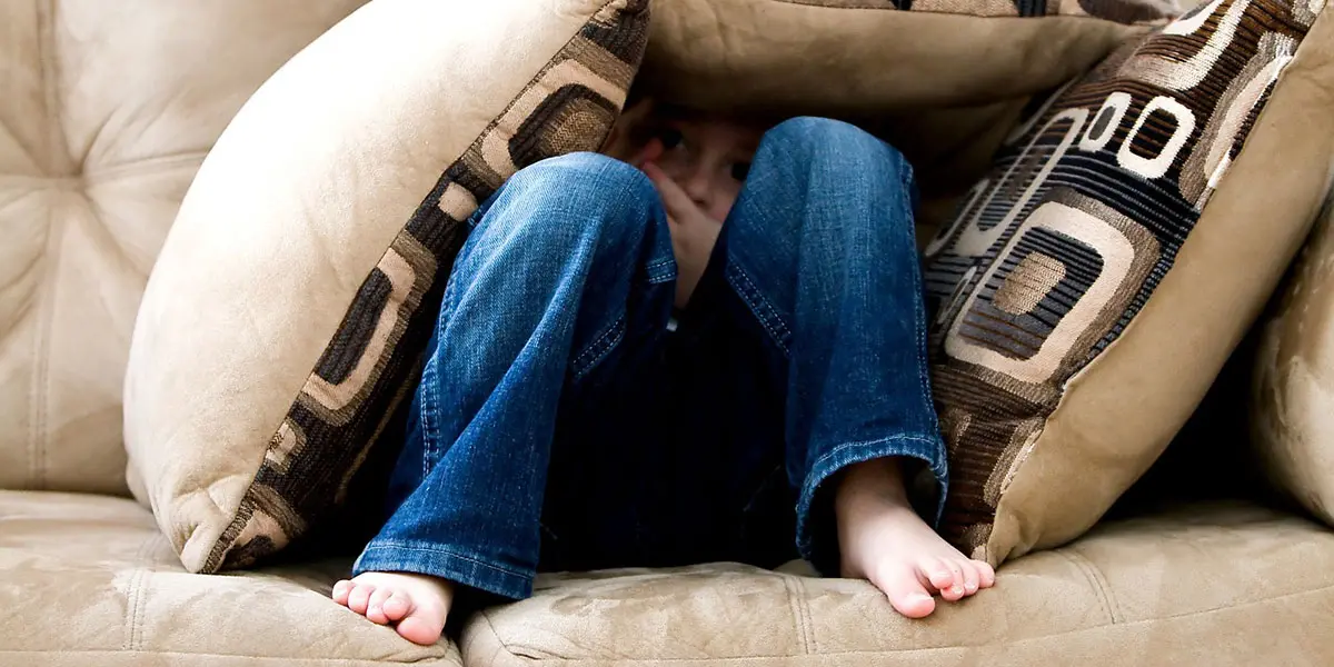 Foto på liten pojke som gömt sig under kuddar i en soffa