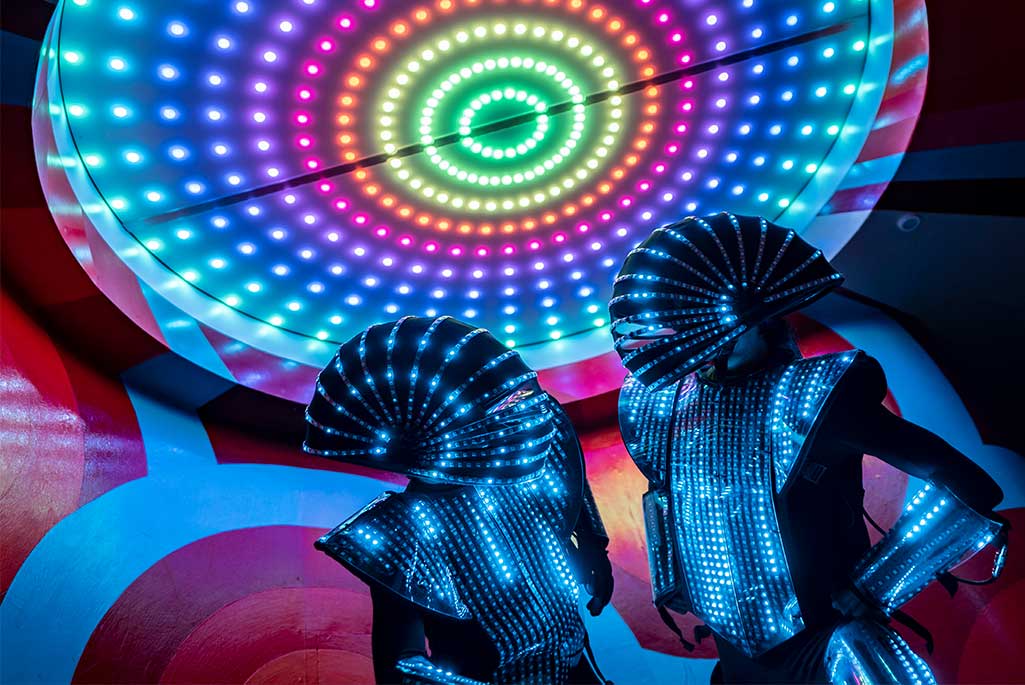 Foto på två personer från gruppen Act of Emotion som har på sig varsin robot dräkt med lysande LED lampor på. 