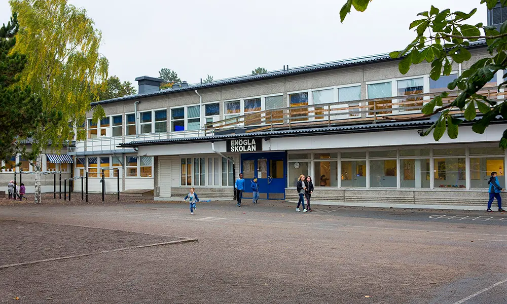 Foto av Enöglaskolan. Det är en gråvit flervåningsbyggnad. 