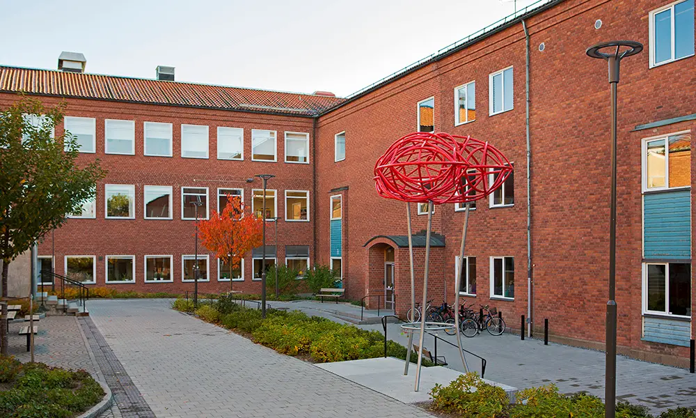 Foto av S:t Iliansskolan. Det är en stor röd tegelbyggnad med flera våningar. 