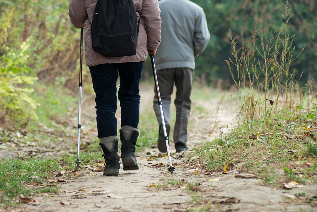 Foto på två personers ben som är ute och vandrar i naturen. En av personerna har gångstavar. 
