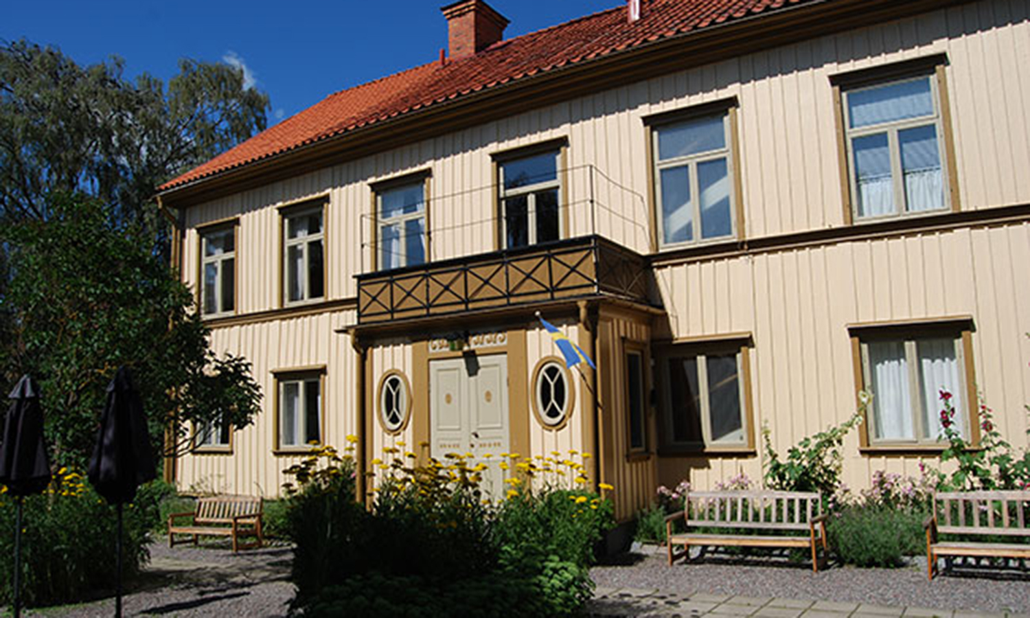 Foto på Westerlundska gårdens fasad. Ett tvåvåningshus i trä med en liten balkong ovanför entrén.