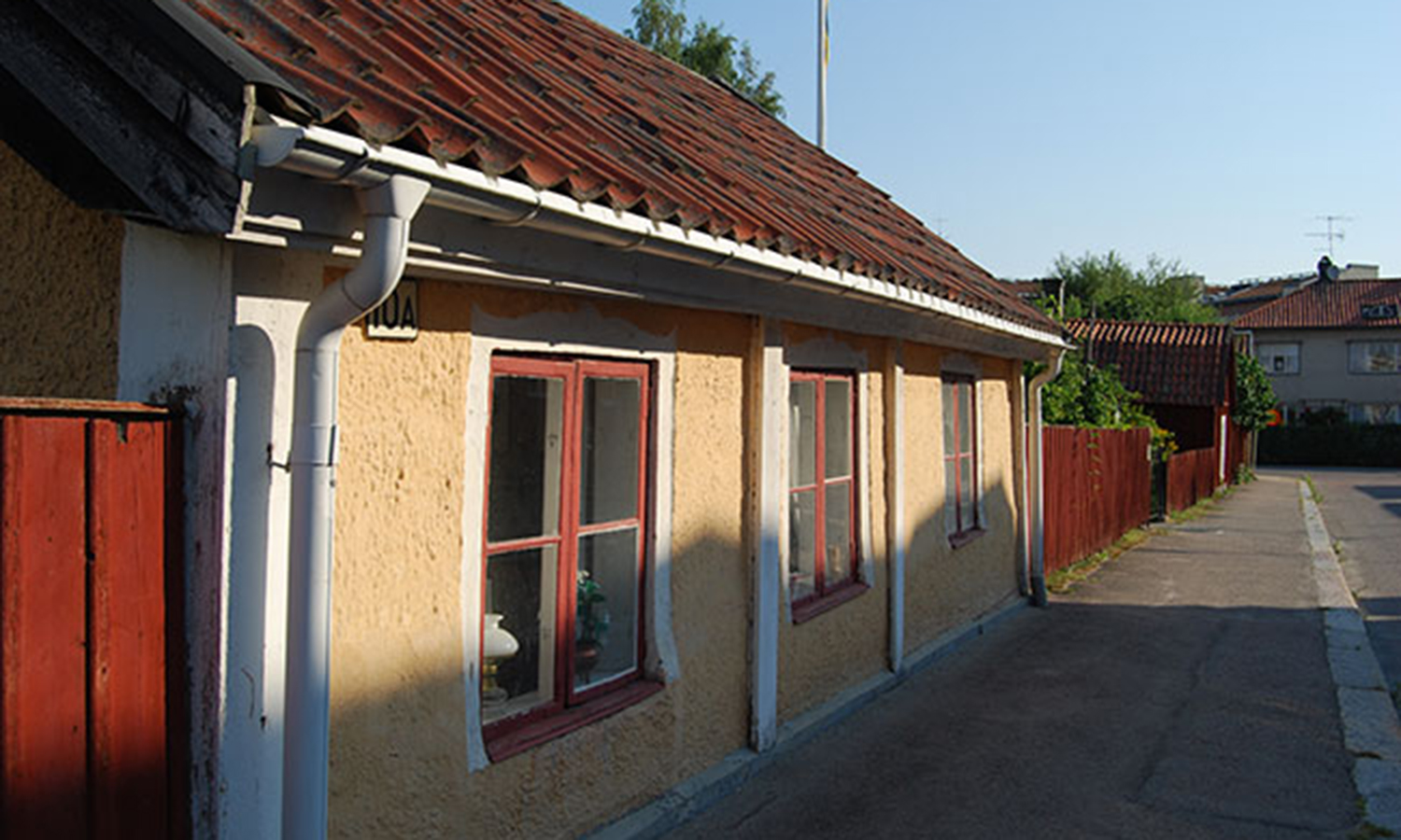Foto på en av  Wallinska gårdens byggnaders fasad. En gul liten stenbyggnad med vita knutar.
