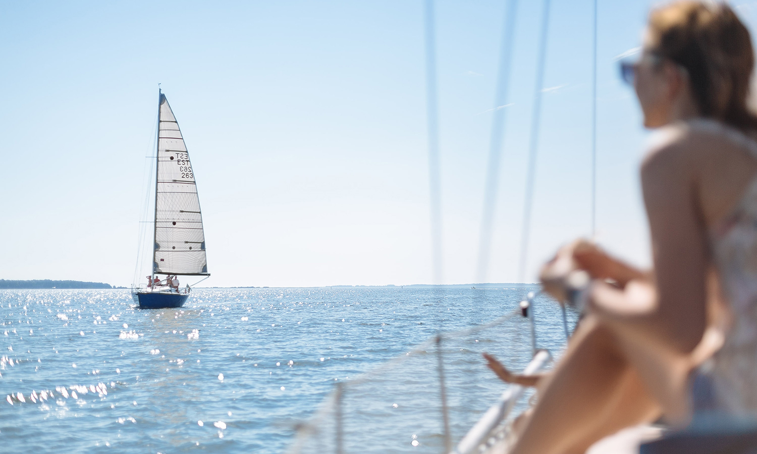 Foto på en kvinna som står på en båt och tittar ut mot vattnet och en annan segelbåt.