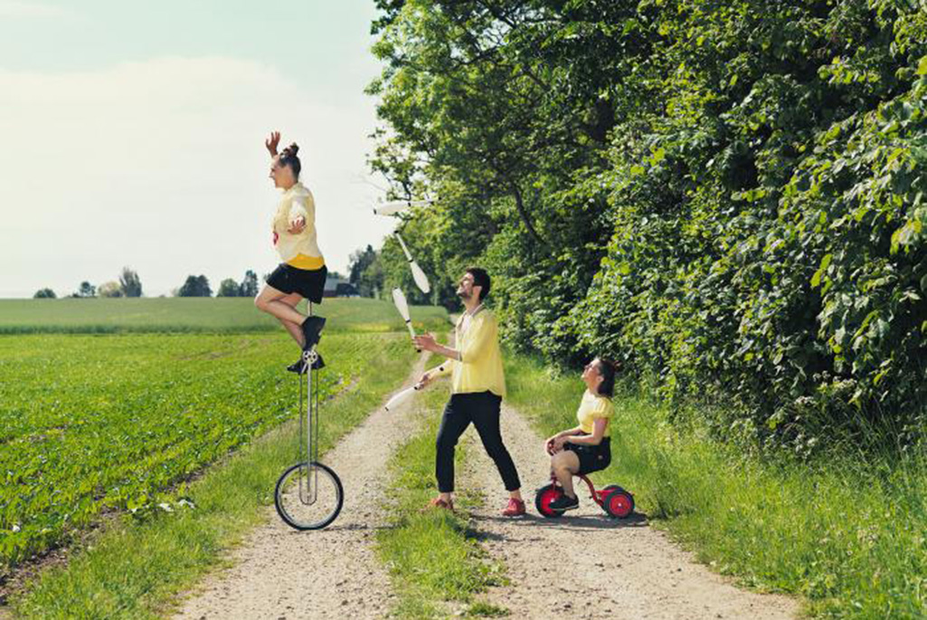 Bild på tre artister från en cykelcirkus, en på enhjuling, en på trehjuling och en gåendes som jonglerar.