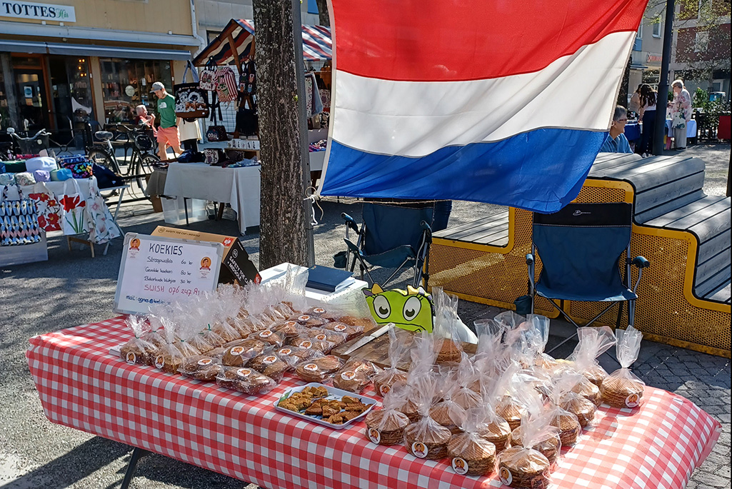 Bild på ett marknadsstånd där det ligger påsar med kakor och där det hänger en holländsk flagga.
