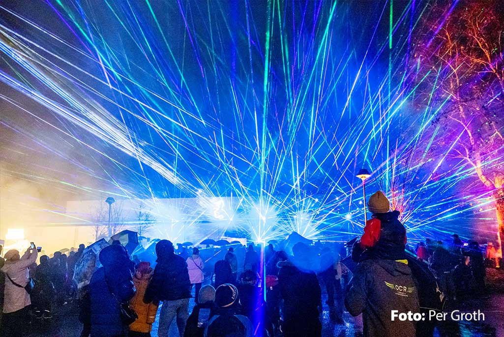 Bild från en lasershow i Enköping där blå ljusstrålar lyser på publiken.