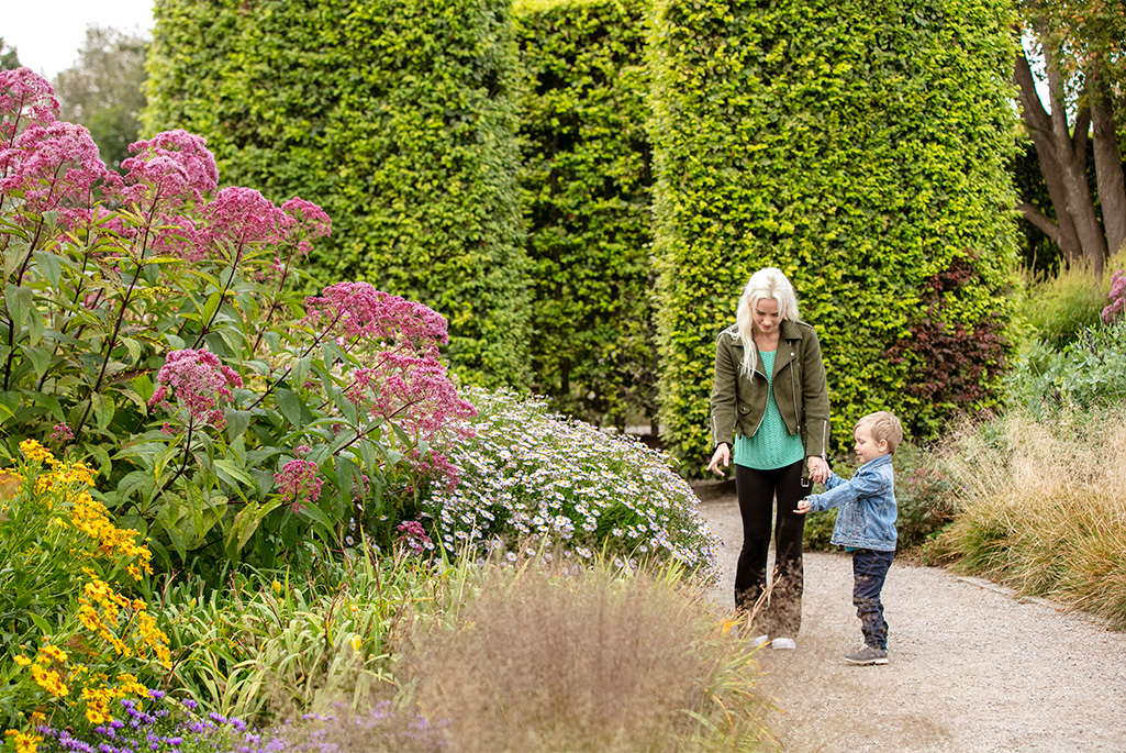 Bild på en kvinna och ett barn som står i en park och tittar på blommor och växter.