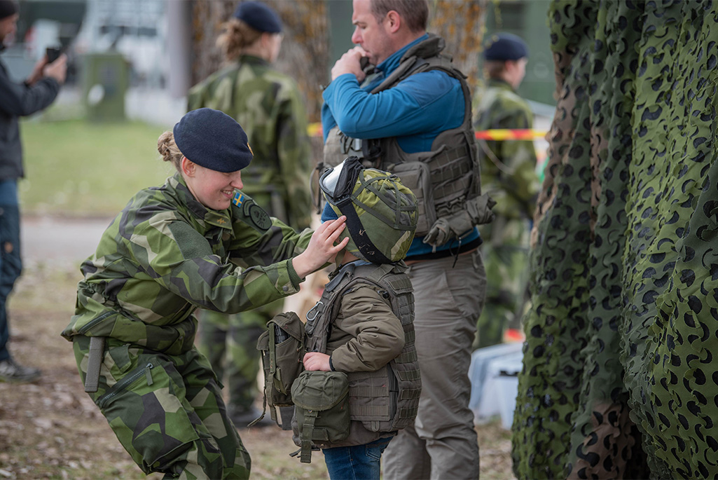 Bild på en militär som hjälper ett barn att prova en militärhjälm.