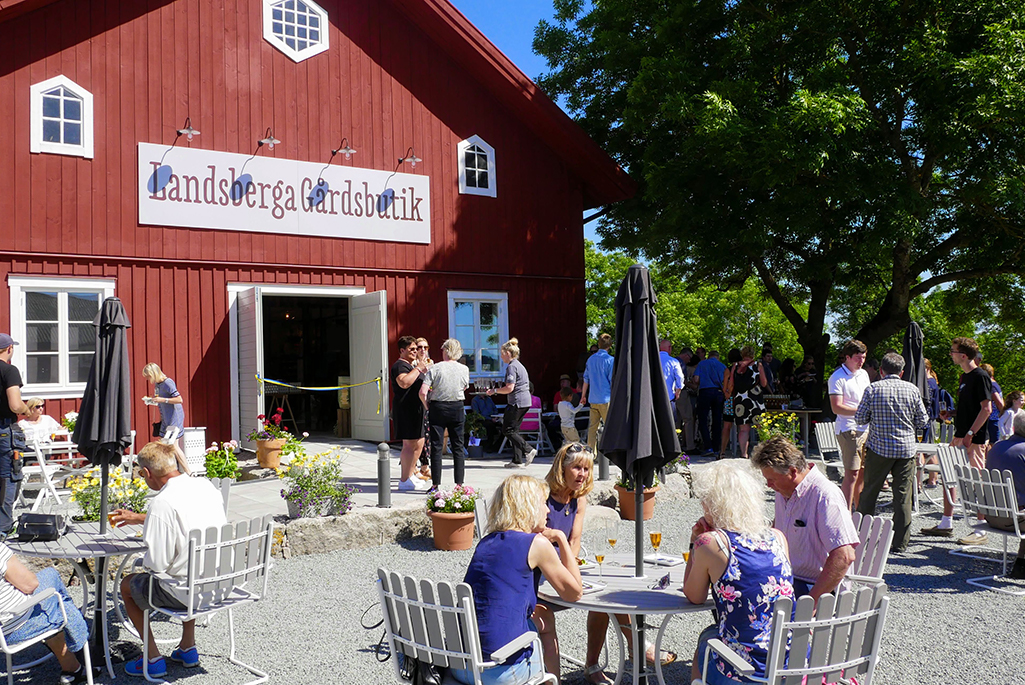 Bild på Landsberga gårdsbutik med människor sittandes vid bord utanför.