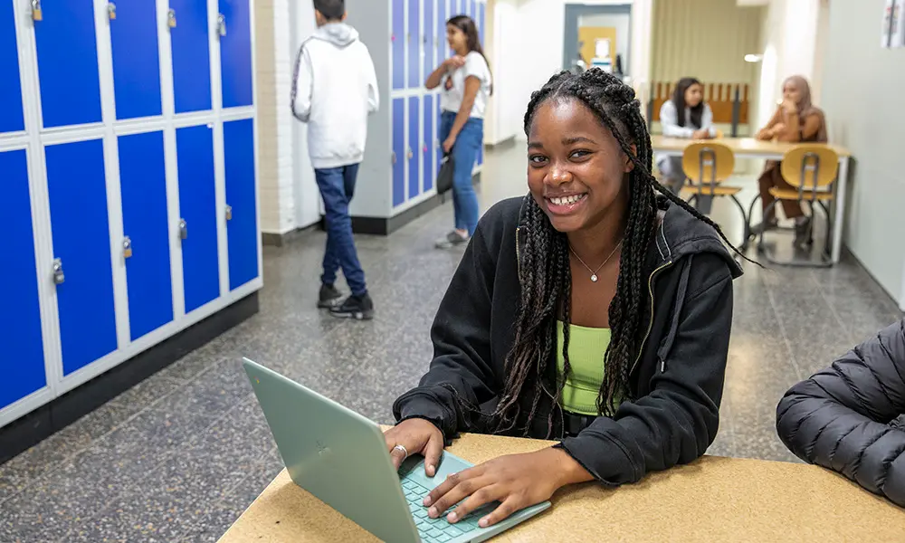 En elev sitter vid sin dator och ler mot kameran.